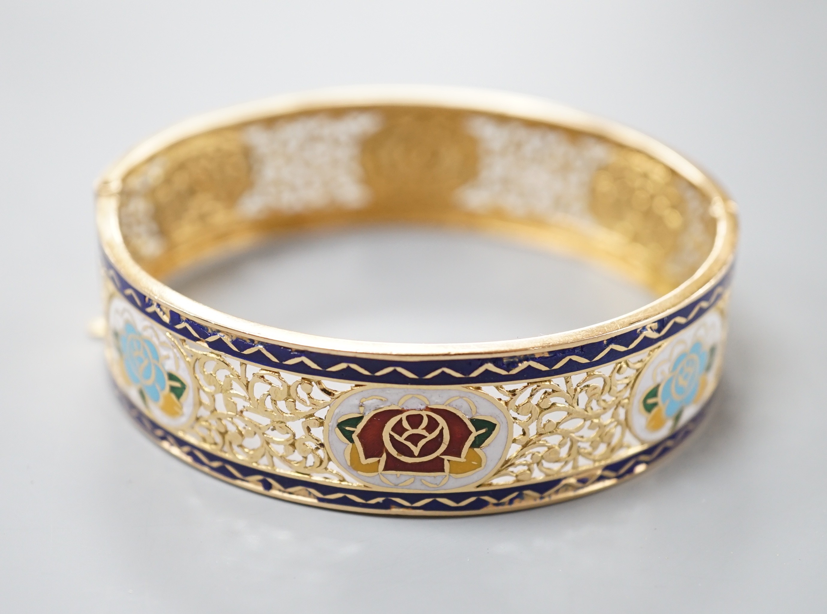 A pierced yellow metal and polychrome enamel set hinged bangle, gross weight 25.3 grams, (enamel a.f.).